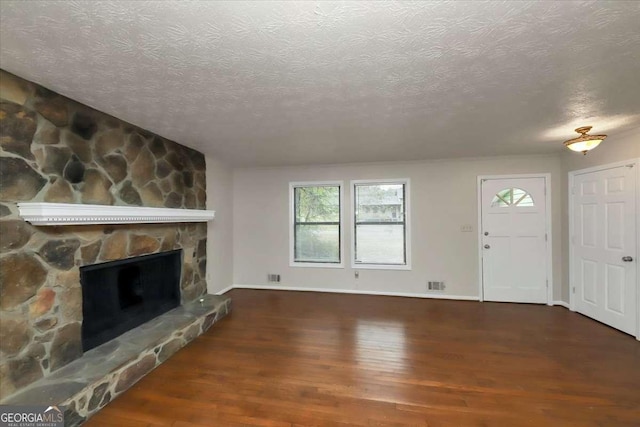 unfurnished living room with a stone fireplace, dark hardwood / wood-style flooring, and a textured ceiling