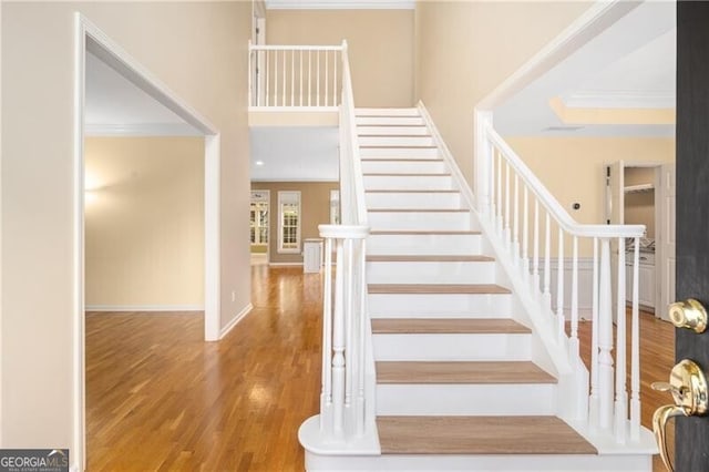 stairway with wood-type flooring and crown molding