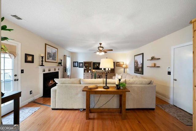 living room featuring ceiling fan, a textured ceiling, and light hardwood / wood-style flooring