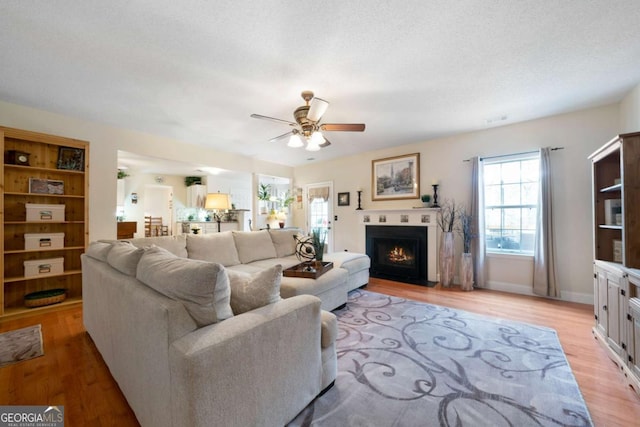 living room with a textured ceiling, light wood-type flooring, and ceiling fan