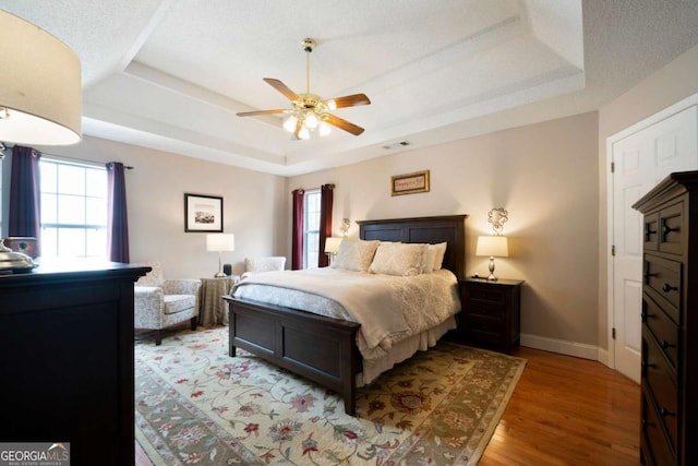 bedroom with hardwood / wood-style floors, a tray ceiling, and ceiling fan