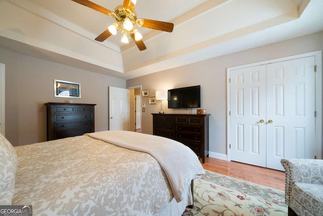 bedroom featuring wood-type flooring, a closet, a tray ceiling, and ceiling fan