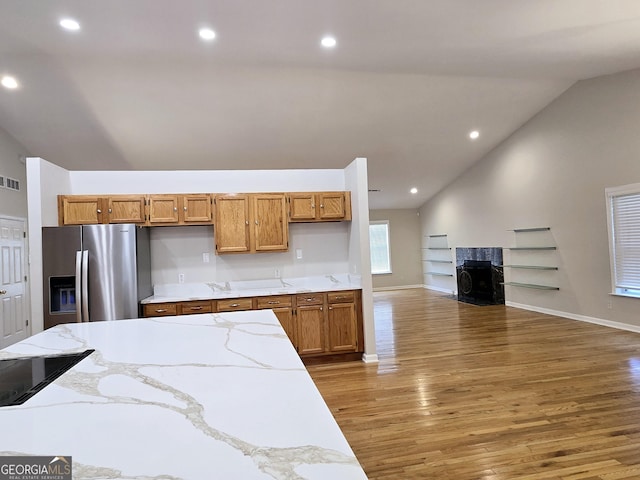 kitchen with vaulted ceiling, hardwood / wood-style floors, a high end fireplace, and stainless steel fridge with ice dispenser