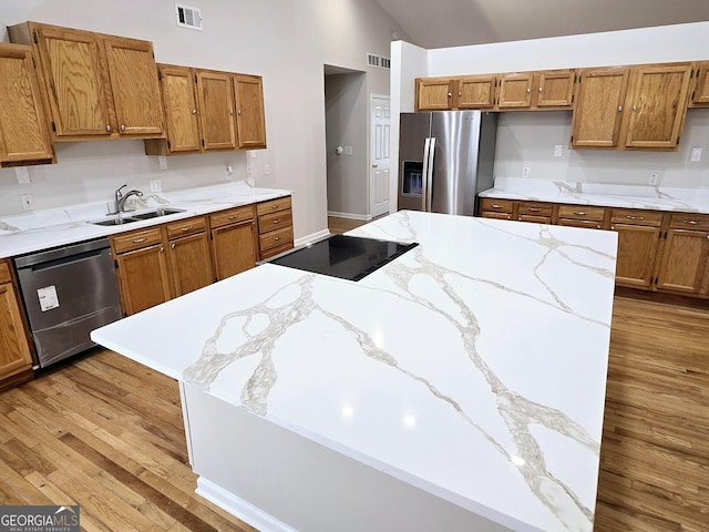 kitchen with appliances with stainless steel finishes, lofted ceiling, sink, light stone counters, and light hardwood / wood-style flooring