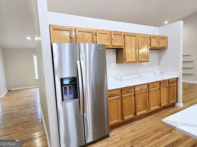 kitchen featuring stainless steel refrigerator with ice dispenser, light stone counters, and light hardwood / wood-style flooring