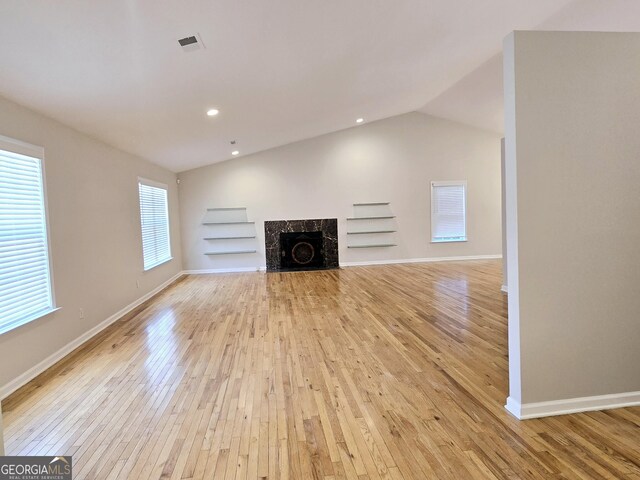 unfurnished living room with built in features, vaulted ceiling, light hardwood / wood-style floors, and a high end fireplace