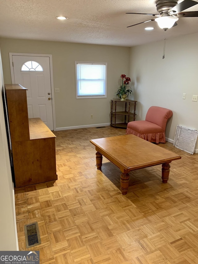 living room with ceiling fan, light parquet floors, and a textured ceiling