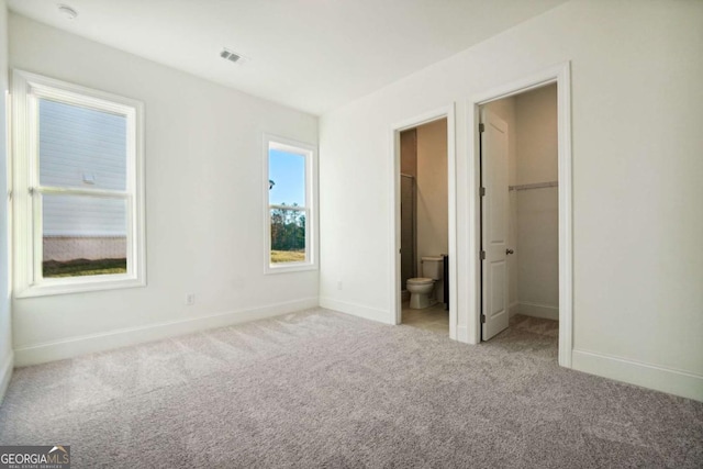 unfurnished bedroom with connected bathroom, light colored carpet, a spacious closet, and a closet