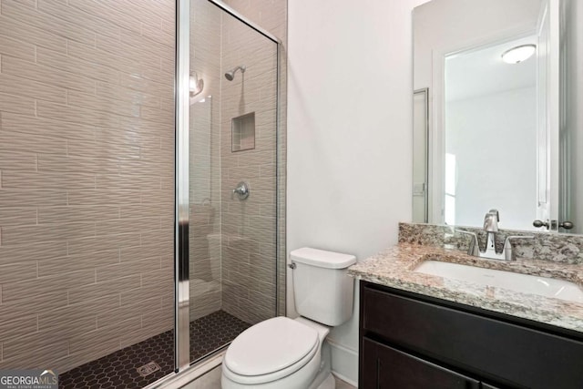 bathroom featuring a shower with door, vanity, and toilet