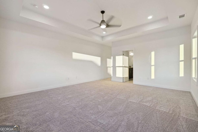 carpeted spare room with a raised ceiling and ceiling fan