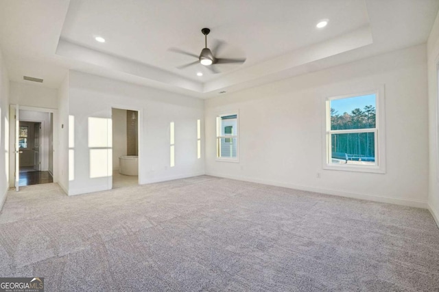 unfurnished bedroom with a raised ceiling, ceiling fan, ensuite bathroom, and light carpet