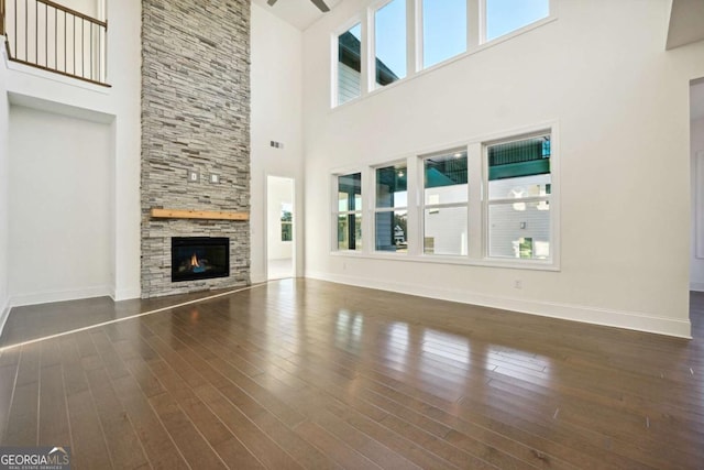 unfurnished living room with dark hardwood / wood-style floors, a fireplace, a healthy amount of sunlight, and a high ceiling