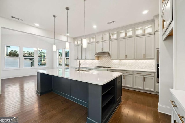 kitchen featuring a center island with sink, sink, appliances with stainless steel finishes, decorative light fixtures, and dark hardwood / wood-style flooring