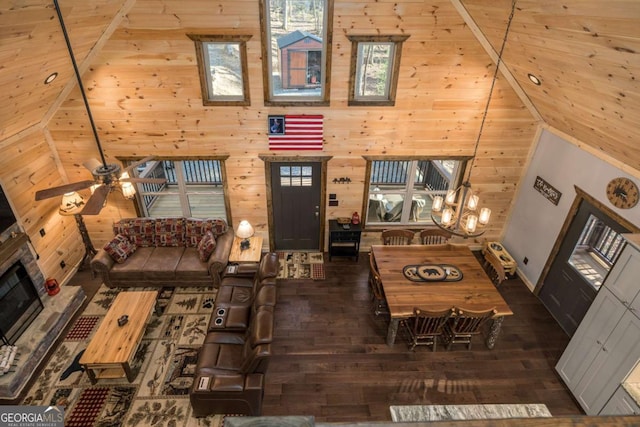 living room featuring wooden ceiling, dark wood-type flooring, ceiling fan with notable chandelier, wooden walls, and a fireplace