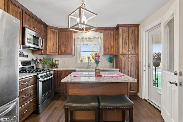 kitchen featuring light stone counters, dark hardwood / wood-style flooring, decorative light fixtures, a kitchen bar, and appliances with stainless steel finishes