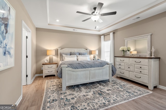 bedroom with a raised ceiling, ceiling fan, and light wood-type flooring