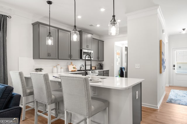 kitchen featuring gray cabinetry, a kitchen breakfast bar, hanging light fixtures, decorative backsplash, and light hardwood / wood-style floors