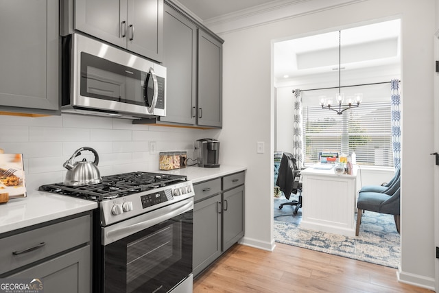 kitchen with decorative backsplash, light wood-type flooring, stainless steel appliances, a chandelier, and gray cabinets