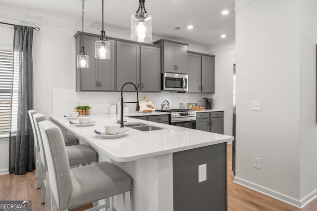 kitchen featuring kitchen peninsula, appliances with stainless steel finishes, sink, hanging light fixtures, and a breakfast bar area