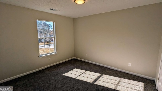 spare room with a textured ceiling and dark colored carpet