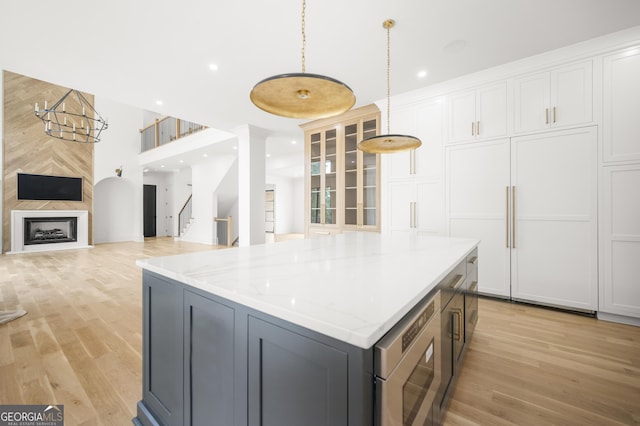 kitchen featuring pendant lighting, a center island, white cabinets, light stone countertops, and light hardwood / wood-style floors