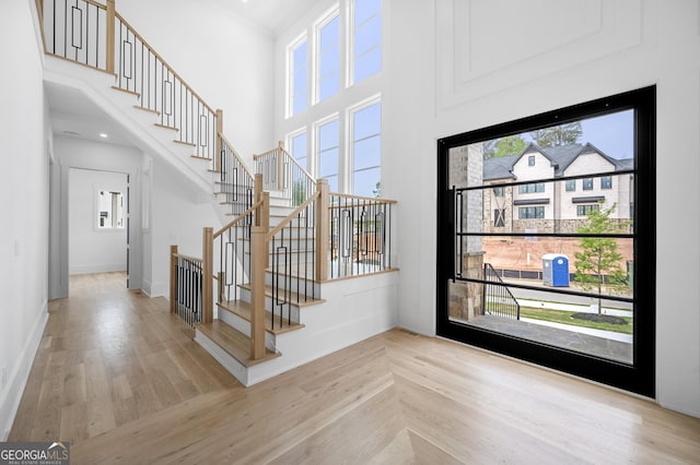 foyer entrance featuring crown molding, light hardwood / wood-style floors, and a high ceiling