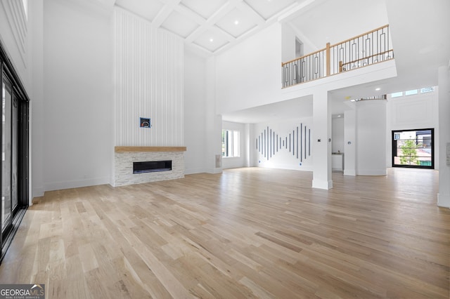 unfurnished living room with beam ceiling, coffered ceiling, a high ceiling, a stone fireplace, and light wood-type flooring