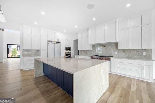 kitchen featuring light stone countertops, stainless steel appliances, a spacious island, light hardwood / wood-style floors, and white cabinetry