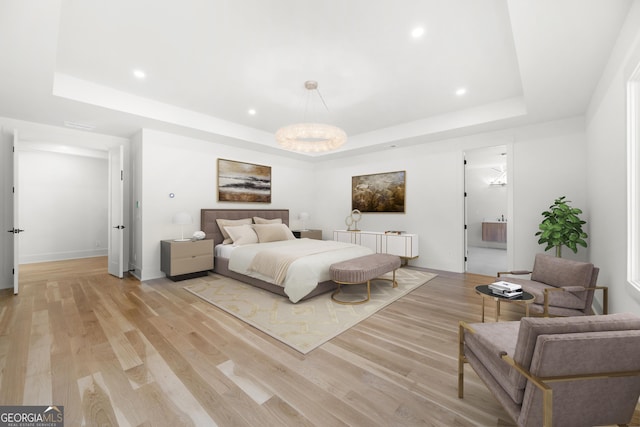 bedroom featuring a raised ceiling, light wood-type flooring, and ensuite bath