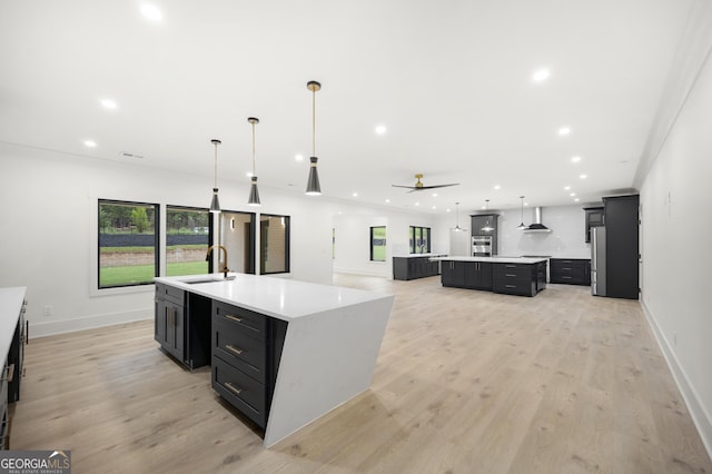 kitchen featuring pendant lighting, ceiling fan, wall chimney exhaust hood, and a large island with sink