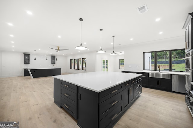 kitchen featuring light wood-type flooring, ceiling fan, a spacious island, sink, and decorative light fixtures