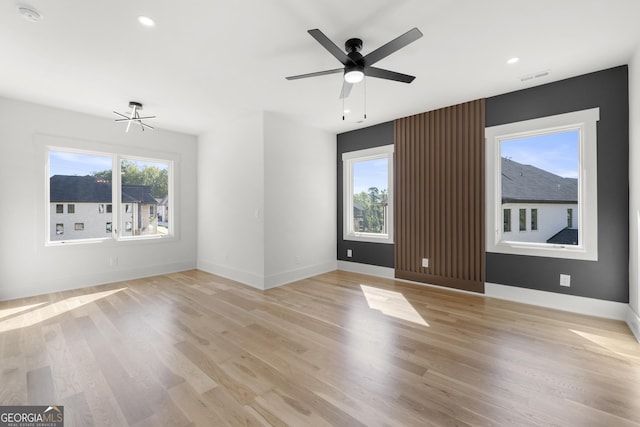 empty room with ceiling fan with notable chandelier and light hardwood / wood-style flooring