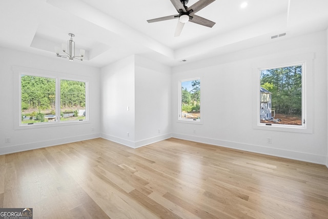 empty room featuring ceiling fan with notable chandelier, light hardwood / wood-style floors, and a tray ceiling