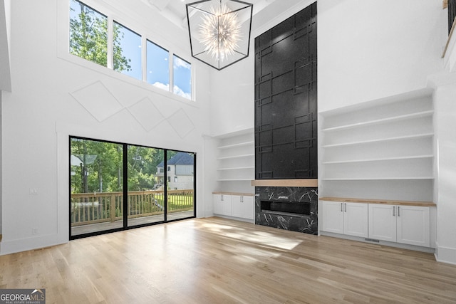 unfurnished living room featuring built in shelves, a high ceiling, light hardwood / wood-style flooring, a high end fireplace, and a notable chandelier