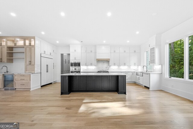 kitchen featuring appliances with stainless steel finishes, light hardwood / wood-style flooring, white cabinets, wine cooler, and a large island