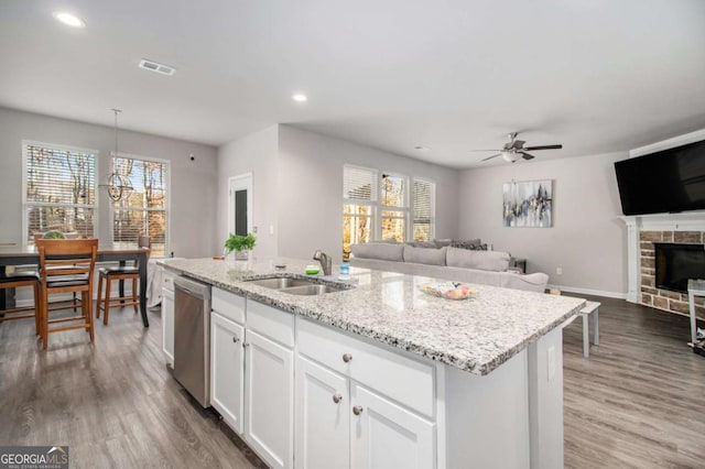 kitchen with dark wood-type flooring, stainless steel dishwasher, a kitchen island with sink, a fireplace, and white cabinets