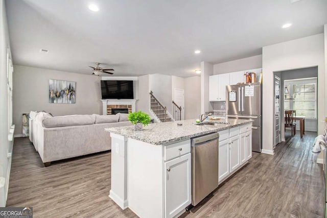 kitchen with wood-type flooring, white cabinetry, stainless steel appliances, and an island with sink