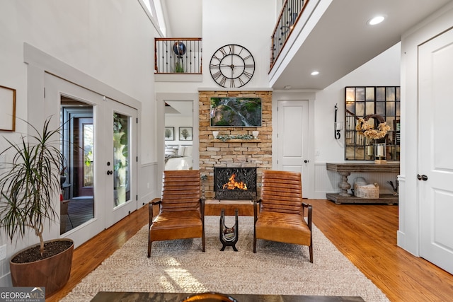 living area with hardwood / wood-style floors, a stone fireplace, a towering ceiling, and french doors