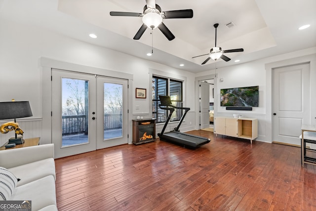 workout area featuring a raised ceiling, ceiling fan, dark hardwood / wood-style flooring, and french doors