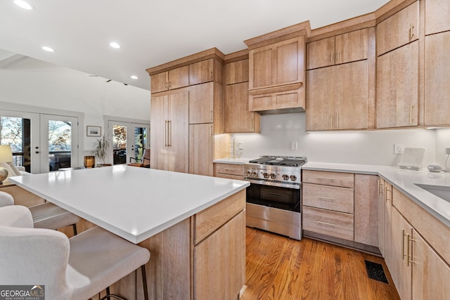 kitchen featuring a breakfast bar, french doors, light hardwood / wood-style flooring, stainless steel gas stove, and a kitchen island