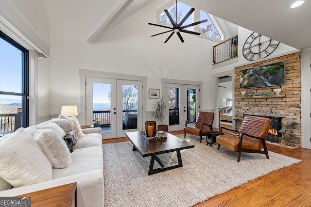 living room featuring ceiling fan, french doors, a stone fireplace, high vaulted ceiling, and hardwood / wood-style floors