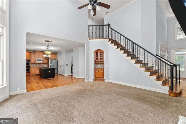 unfurnished living room with crown molding, a towering ceiling, sink, and light carpet