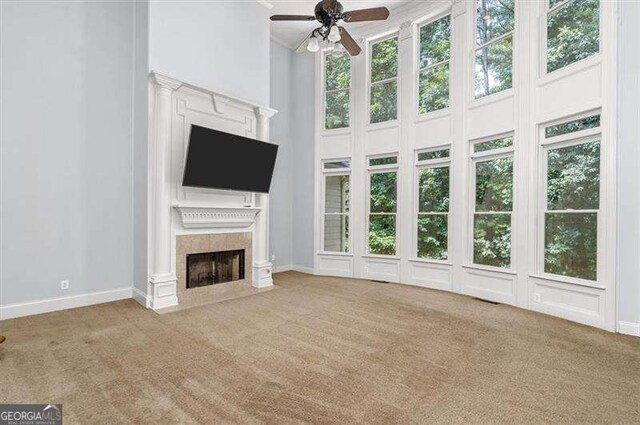 unfurnished living room featuring ceiling fan, a towering ceiling, light colored carpet, and a fireplace