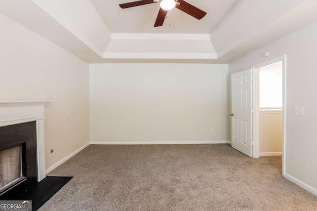 unfurnished living room with ceiling fan, a raised ceiling, and light carpet