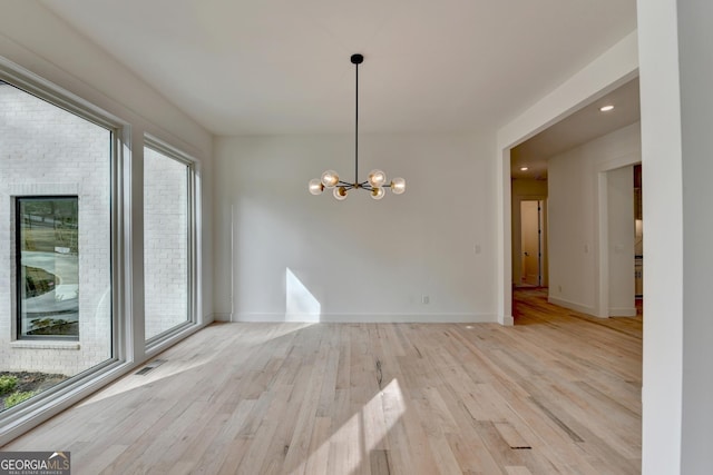 unfurnished dining area featuring an inviting chandelier and light hardwood / wood-style floors