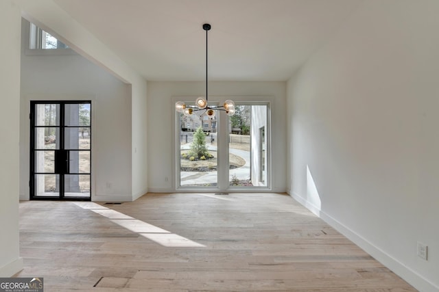 unfurnished dining area with an inviting chandelier and light hardwood / wood-style flooring