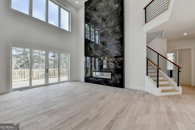 unfurnished living room featuring a towering ceiling, a premium fireplace, and light hardwood / wood-style floors