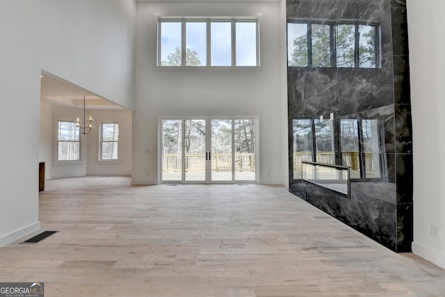 unfurnished living room featuring a high ceiling, a chandelier, light wood-type flooring, and french doors