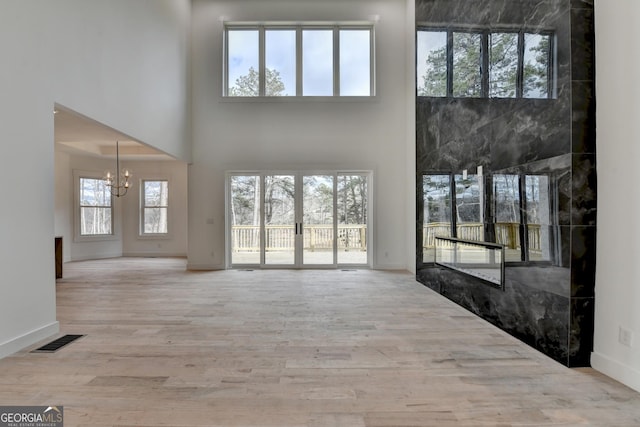 unfurnished living room with a wealth of natural light, a notable chandelier, and light wood-type flooring