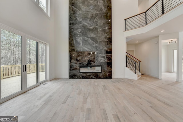 unfurnished living room featuring a towering ceiling, a fireplace, and light hardwood / wood-style floors